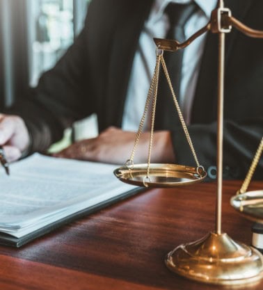 Person signing documents next to lawyers scales